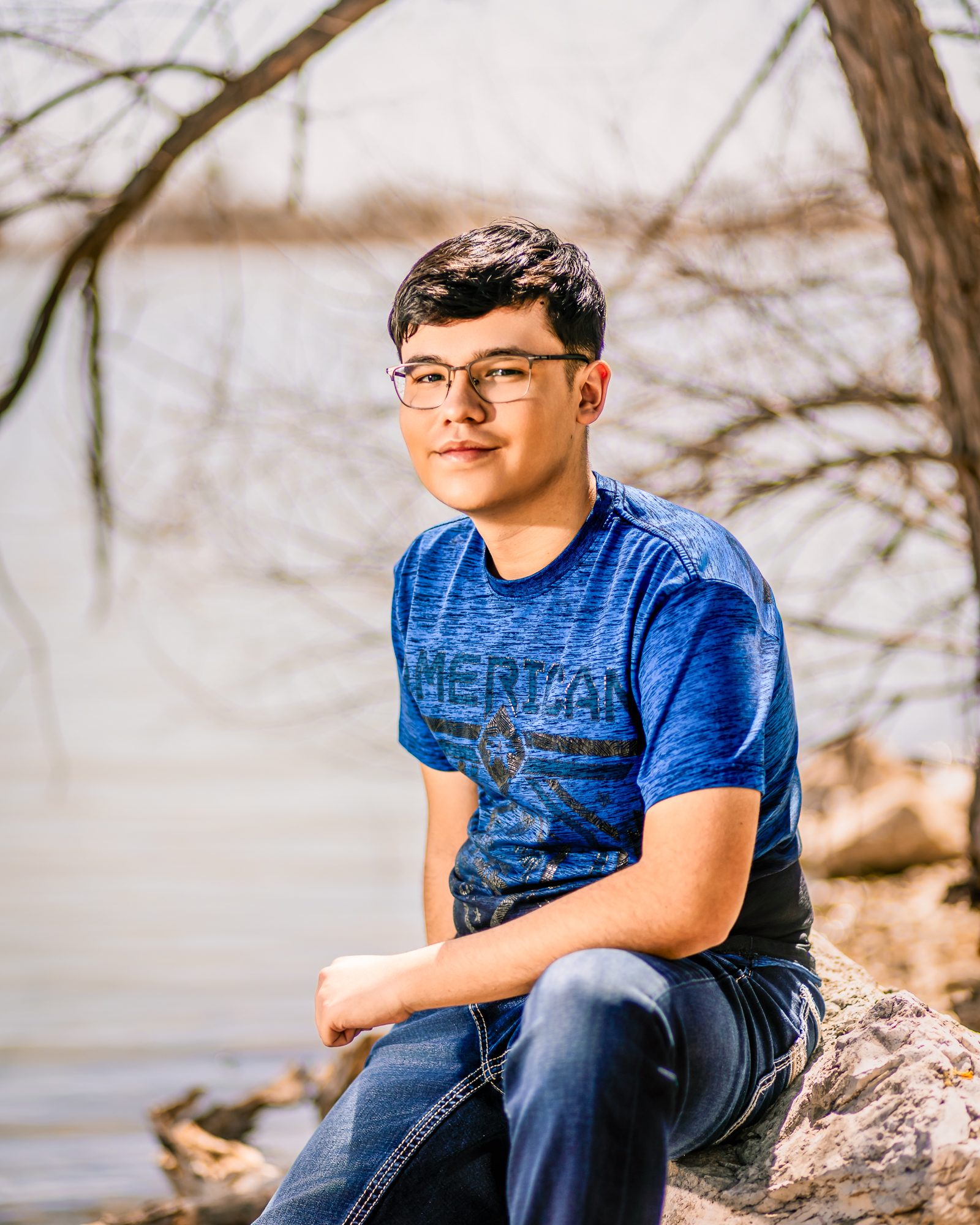 young man sitting near a river with the sun shining behind him